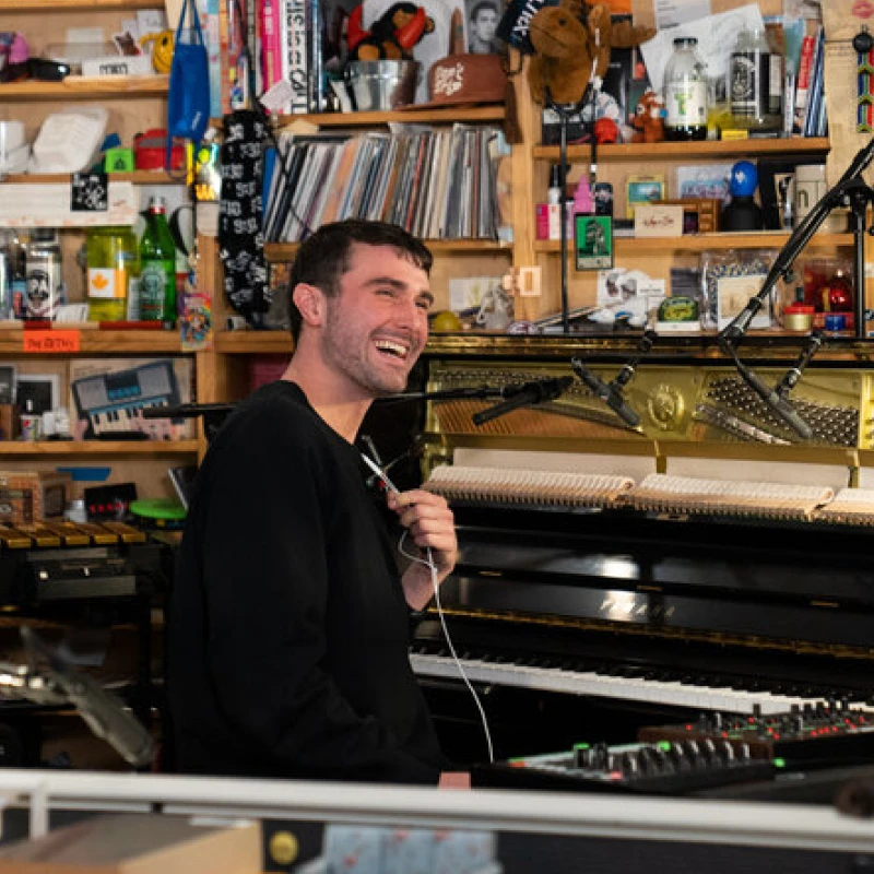 A photograph of Fred again... in the studio smiling looking back towards someone out of frame.